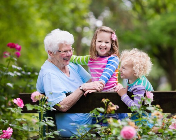 Ältere Dame sitzt mit zwei Kindern auf einer Parkbank und lacht | © famveldman - Fotolia